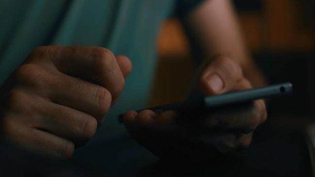 Close up of hands using smartphone in dark home office interior, low key footage