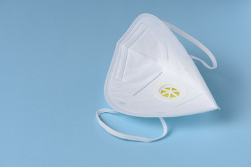 A disposable respirator with breathing valve isolated on light blue background.