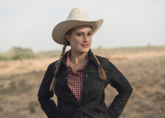 Smiling retro 1950s cowgirl in jeans jacket in countryside.