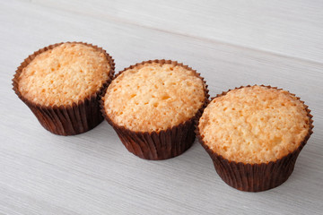 Three orange cupcake without cream on a white wooden table. Picture for a menu or a confectionery catalog. Top view.