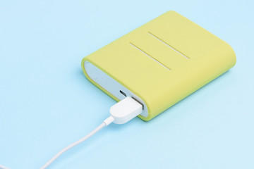 Fototapeta premium A yellow colored portable power bank isolated on light blue background.