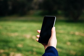 A smart phone held by a female hand on blurred green natural background.