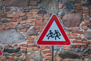 Road sign caution children over stone wall  background.
