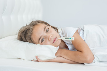 sick girl lying in bed with a thermometer in mouth