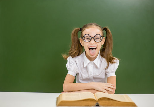 Funny  nerd student with open book showing tongue out on the background of a school board