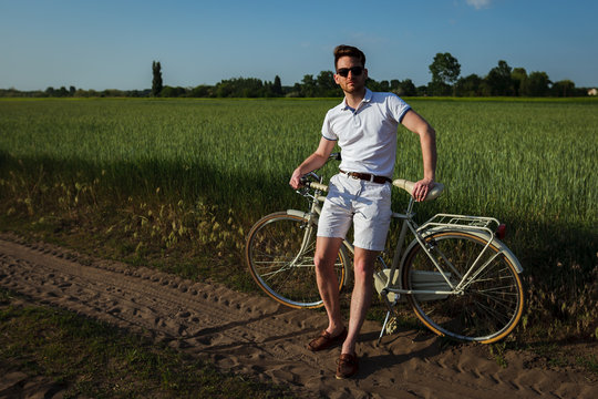 Handsome man posing with his retro italian bicycle on green field