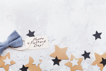 Happy Fathers Day background with greeting tag, bowtie and star confetti on table top view. Flat lay composition.