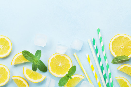 Lemon slices, ice, colorful straw and mint leaves on blue table top view. Ingredients for summer cocktail and lemonade. Flat lay.
