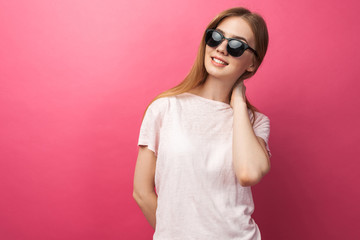 Beautiful young blonde girl in glasses standing on pink background wearing jeans, pink top smiling snow white smile, wearing black glasses and looking perfect promotional photo