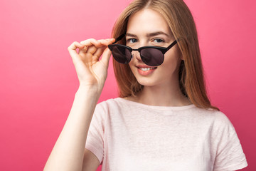 Beautiful young blonde girl in glasses standing on pink background wearing jeans, pink top smiling snow white smile, wearing black glasses and looking perfect promotional photo
