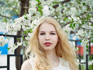 Naklejka premium Close up of blonde student girl posing in blossoming cherry tree and enjoying warm sun light, recreation and relaxation on spring holiday