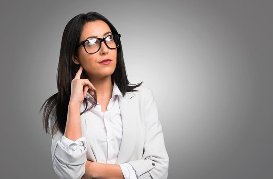 Pretty woman with glasses thinking on grey background