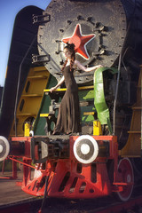 A woman in a vintage black dress posing on an old locomotive. Portrait of a fashionable woman in retro style.