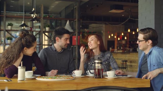 Happy and attractive group of female and male friends are chatting and laughing together in a small cafe or pizza house. Communication and food service concept.