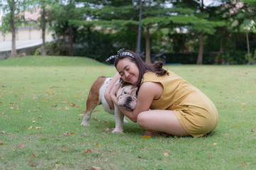 woman smile and hug white english bulldog on green grass in the garden.