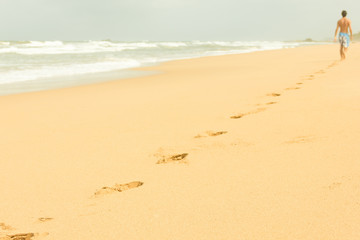 Footprints on empty beach with man on background in a cloudy morning in Bentota, Sri Lanka.