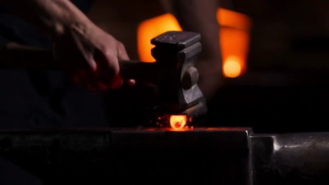 Get out of the furnace hot metal to make a sword war. Master of ancient art creates metal products. In slow motion blacksmiths hammer on red metal flying sparks.