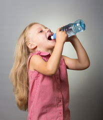 Beautiful little girl with long hair drinking water from bottle on gray