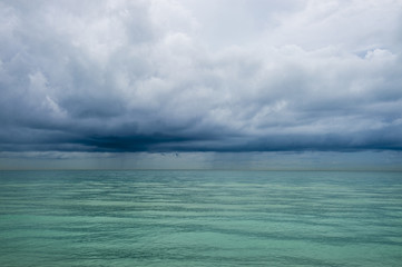 Calm tropical turquoise sea under darkening storm storm clouds on the horizon