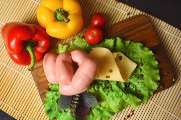 Sausages with cheese on a wooden board with lettuce, basil, cherry tomatoes and paprika.