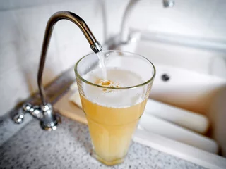  Slecht water wordt uit de kraan in het glas gegoten. Vuil water kan een bron van ziekte zijn © Tricky Shark