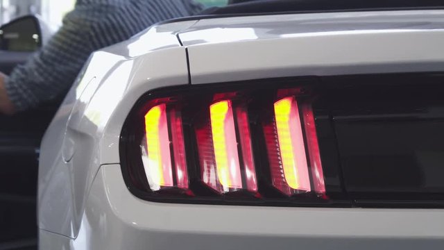 Close up shot of car lights flashing as a male driver getting into the car at the dealership showroom. Mosern cars for sale. Automobile rental service. Technology, automotive industry concept.