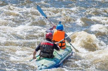 Rafting, kayaking. Two sportsmen in sports equipment are sailing on a rubber inflatable boat in a boiling water stream. Teamwork. Water splashes close-up. Extreme sport.