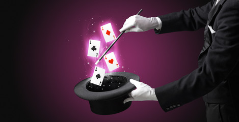 Magician with white gloves conjuring playing cards from a cylinder with magic wand