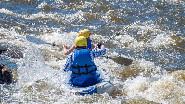 Rafting, kayaking. Two sportsmen in sports equipment are sailing on a rubber inflatable boat in a boiling water stream. Teamwork. Water splashes close-up. Extreme sport.