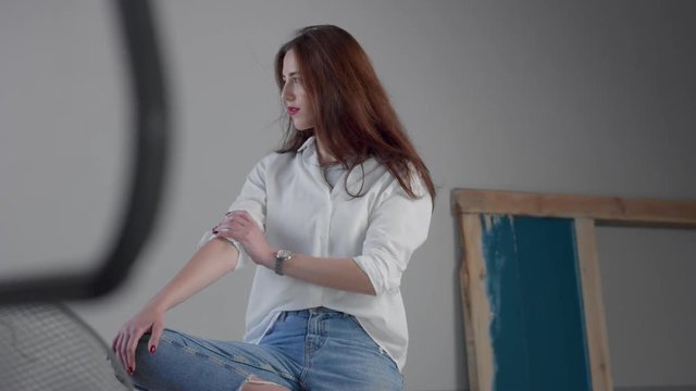 woman in industrial studio wears jeans and white shirt blowing long hair rose bright lips. Classick jeans outfit