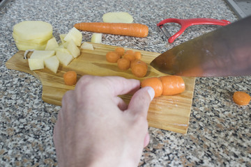 Cutting potatoes and carrots in a kitchen with a big knife