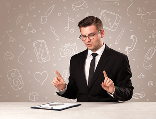 Young handsome businessman sitting at a desk with white mixed media icons behind him
