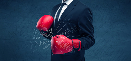 A confident businessman standing in red boxing gloves on his hand in front of blue wall background...
