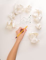 Female hand next to a few crumpled paper balls drawing a progress chart