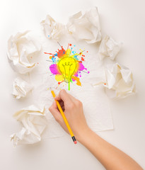 Female hand next to a few crumpled paper balls drawing a colorful lightbulb