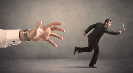 Young miniature businessman running from a big hand with grey background