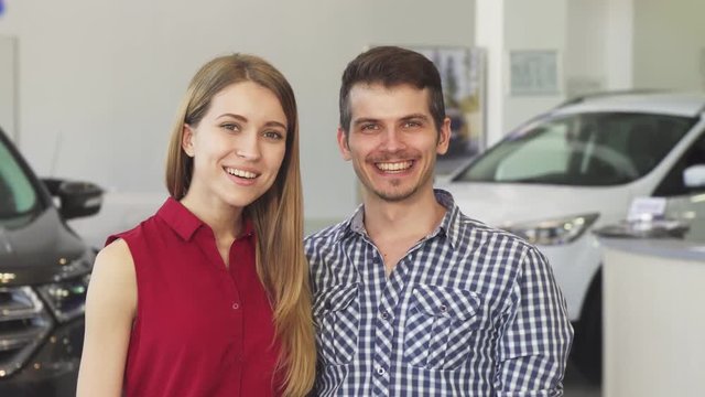 Portrait of a handsome man and his gorgeous girlfriend smiling happily embracing showing car keys to the camera, posing at the dealership showroom. Consumerism, driving, ownership.