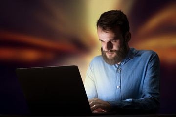 Young handsome businessman working late at night in the office with warm lights in the background