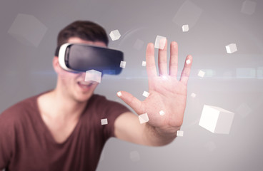 Young impressed man wearing virtual reality goggles with grey cubes around him 