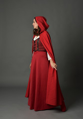 Naklejka premium full length portrait of woman wearing red fantasy costume with cloak, standing pose on grey studio background.
