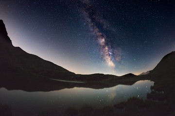 Milky Way arch and starry sky reflected on lake at high altitude on the Alps. Fisheye scenic...