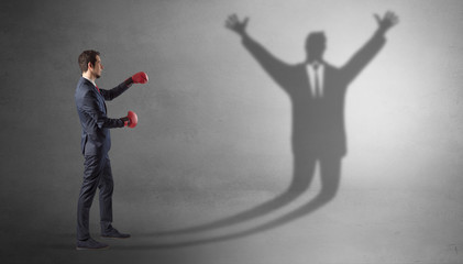 Fototapeta premium Businessman with boxing gloves fighting with disarmed businessman shadow 