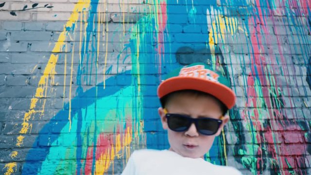Portrait of a 5-year-old street dancer, A cool 5 year old child dances in sunglasses near a brick wall with graffiti