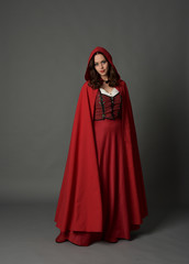 full length portrait of woman wearing red fantasy costume with cloak, standing pose on grey studio background.