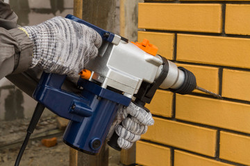 Repairman hands with a puncher. The guy with the drill in his hand mounts the wall.