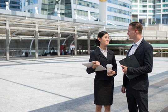 Asian business woman wear suit holding document and talk about business future with Caucasian businessman at the place outside building in the city