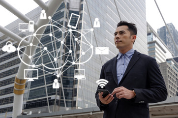 young handsome asian business man wearing modern black suit reading information about finance news with mobile tablet and graphic network icon, investment, technology, internet, successful concept