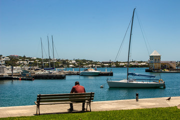 Fototapeta na wymiar Barr's Park, Hamilton, Bermuda. Boat moored at dock with man sitting on a bench