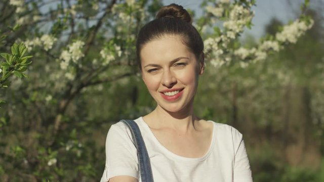 Crop young attractive female smiling and looking at camera with blossoming tree on background.