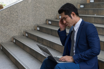 A businessman sit on the stairs and his hands clasped head,the feeling of stressed, sadness or displeasure caused by the non fulfillment of one's hopes or expectations.